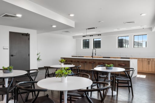 a room with white tables and chairs and a kitchen counter in the background